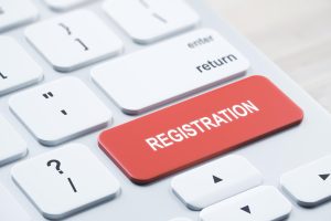 close-up-red-registration-button-white-keyboard-placed-blurry-wooden-desktop-concept-3d-rendering